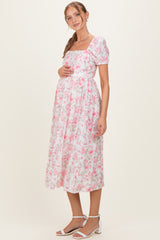 woman wearing a pink floral maternity dress with puff sleeves and holding her baby bump