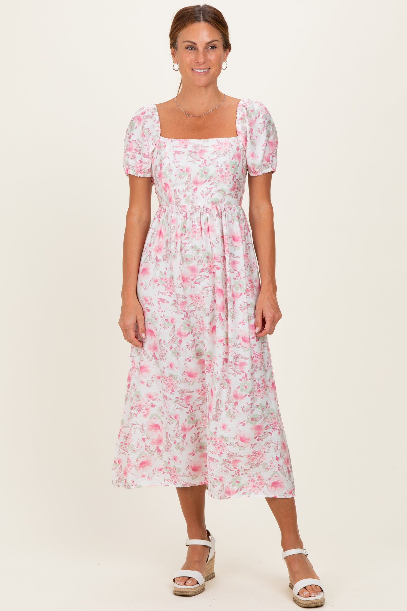woman wearing a white floral midi dress with puff sleeves and a square neckline, standing against a neutral background