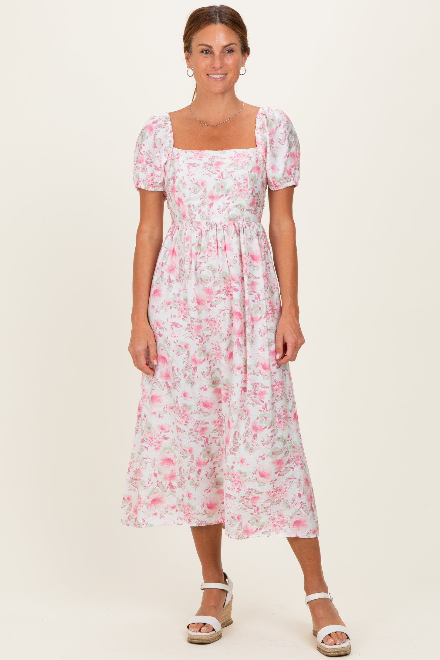 woman wearing a white floral midi dress with puff sleeves and a square neckline, standing against a neutral background