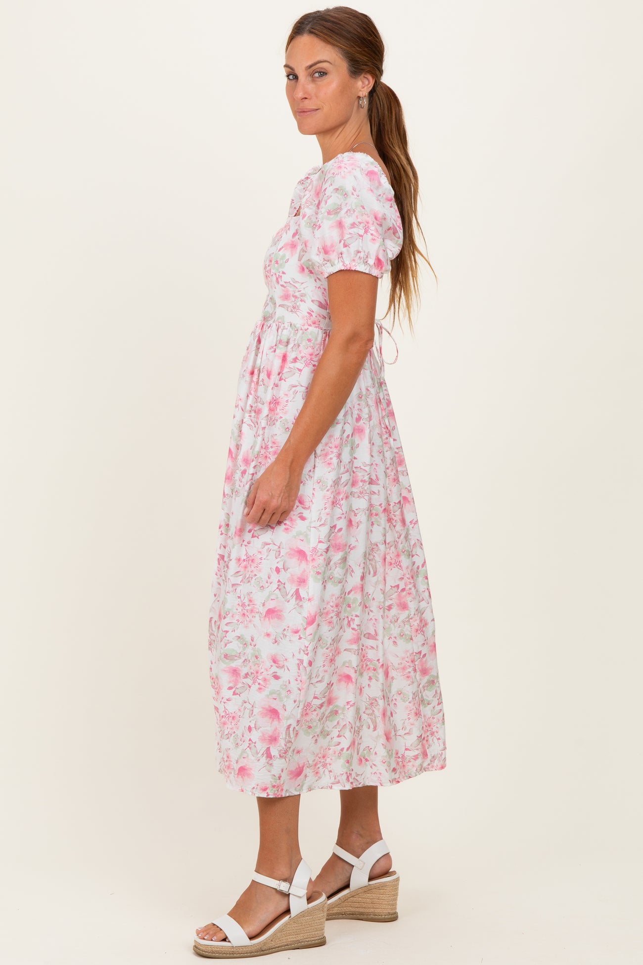 woman wearing a floral pink midi dress with short puff sleeves and a fitted waist, styled with white wedge sandals