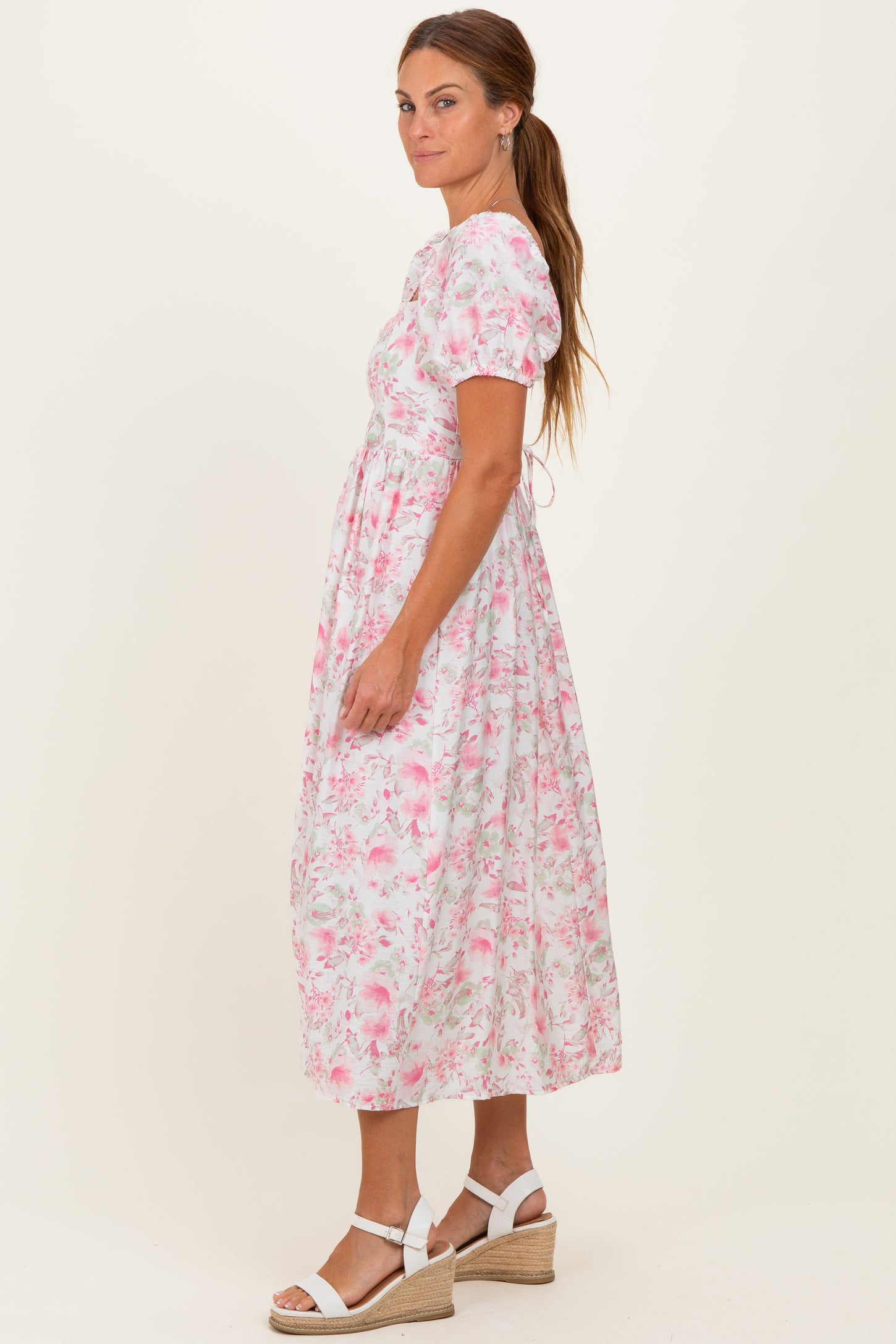 woman wearing a floral pink midi dress with short puff sleeves and a fitted waist, styled with white wedge sandals
