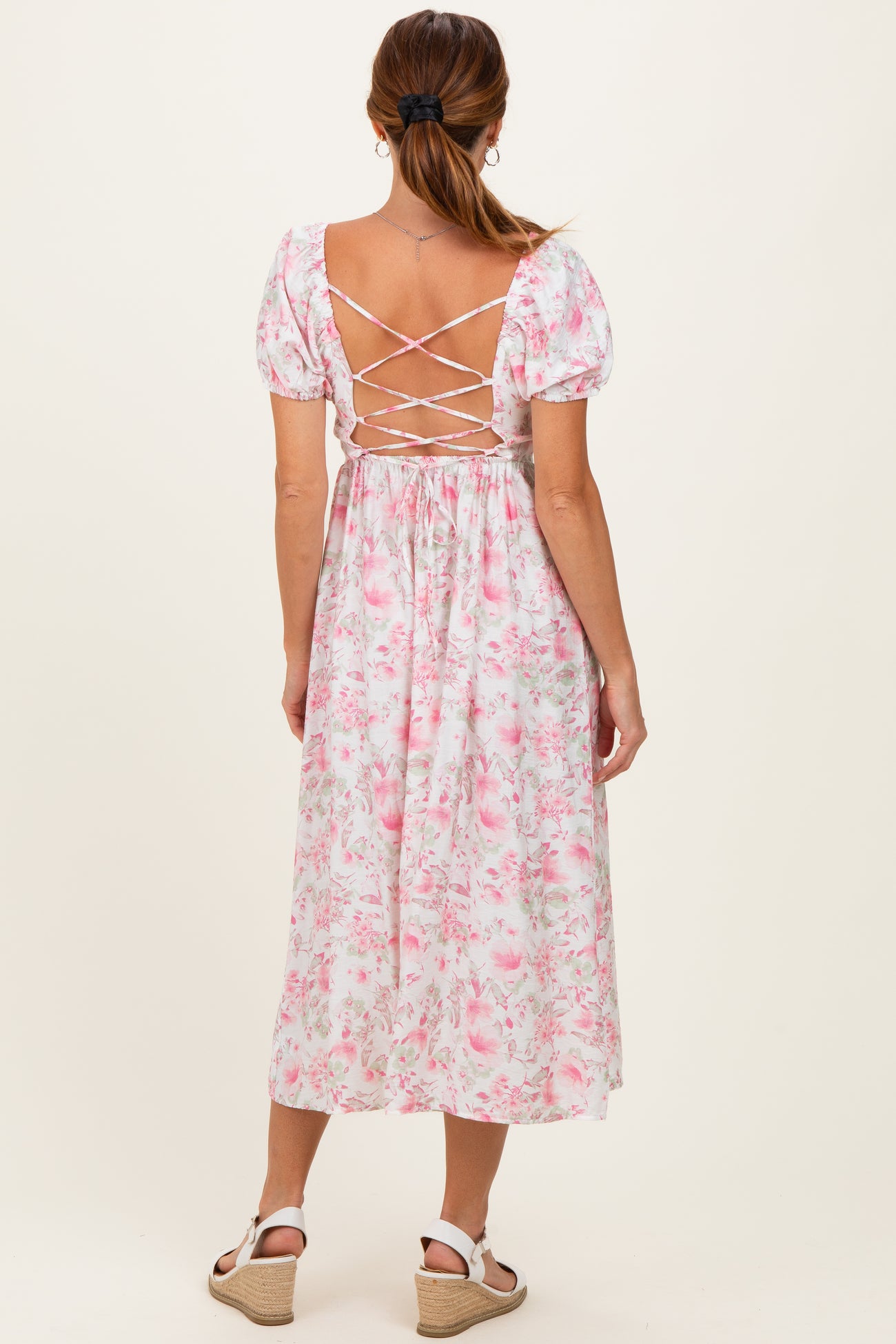 woman wearing a pink floral midi dress with puff sleeves and crisscross back detail
