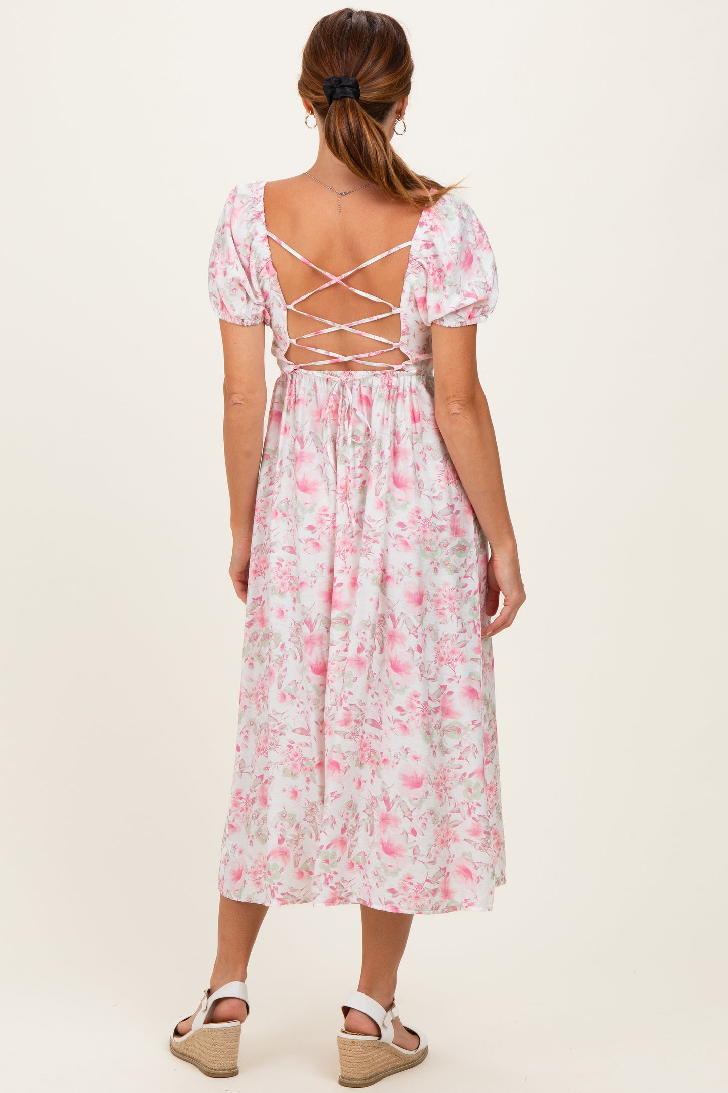 woman wearing a pink floral midi dress with puff sleeves and crisscross back detail