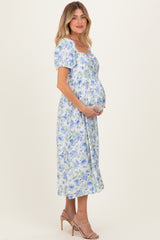 woman wearing a blue floral maternity dress with puff sleeves and holding her baby bump