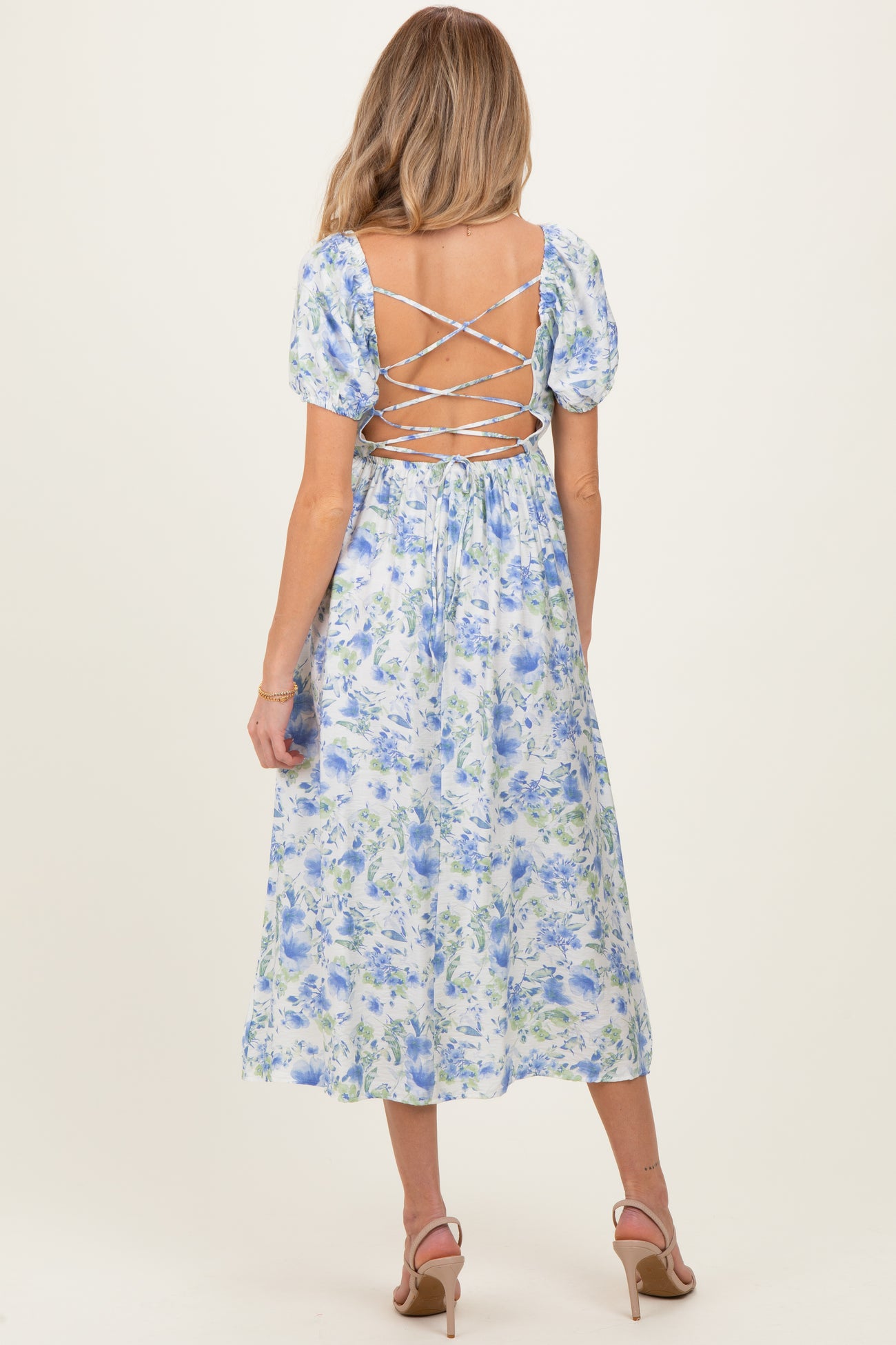 woman wearing a floral backless maternity dress with puff sleeves and lace-up detail, showcasing a baby bump