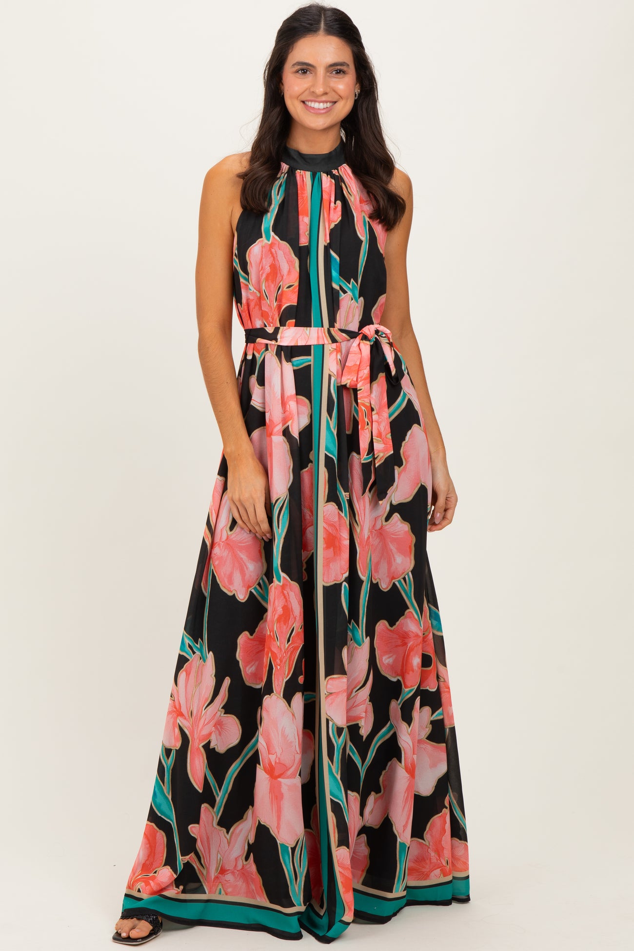 woman wearing a black maxi dress with pink floral print and a halter neckline, featuring a tied waist belt
