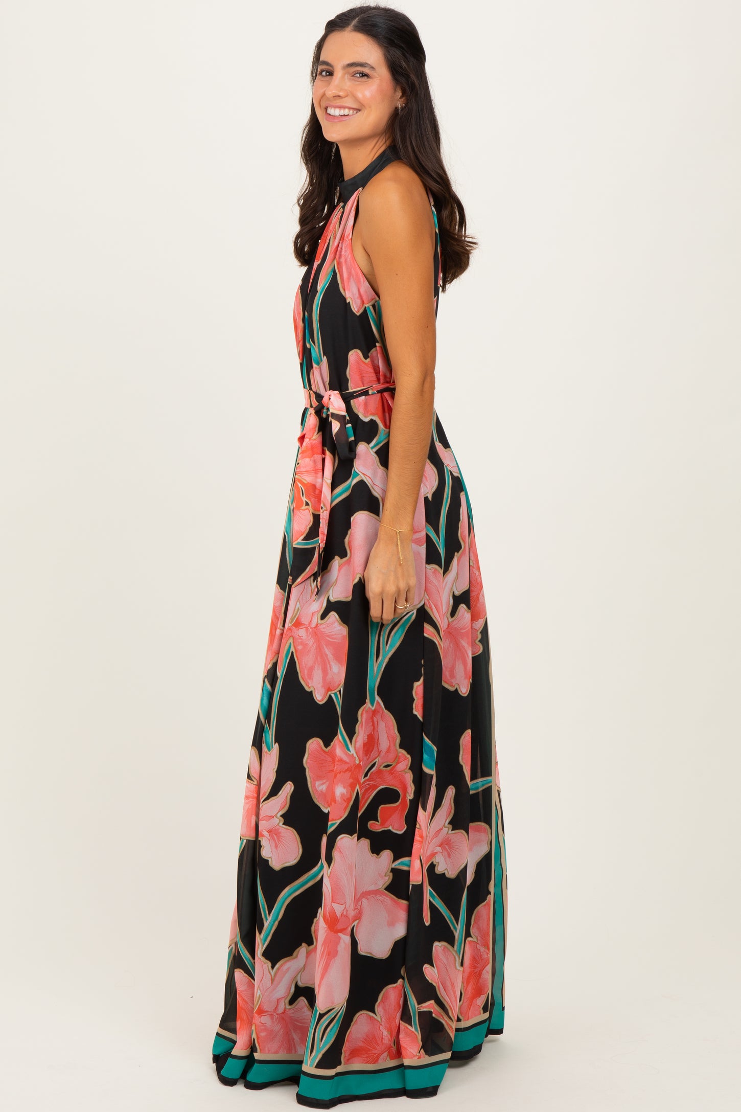 woman wearing a black maxi dress with a vibrant pink floral pattern and a belted waist, posing from the side