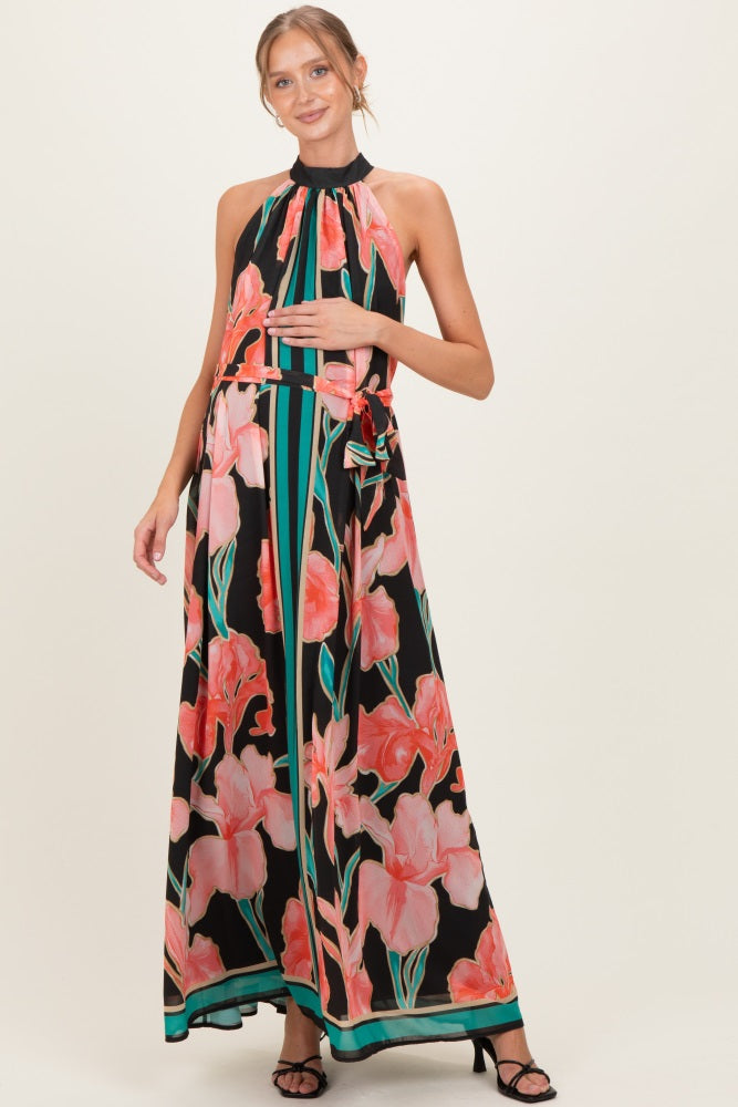 woman wearing a black floral maxi maternity dress with a halter neck and a tied waist, holding her baby bump