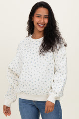 woman wearing a cream floral print maternity sweatshirt and blue jeans, displaying her baby bump