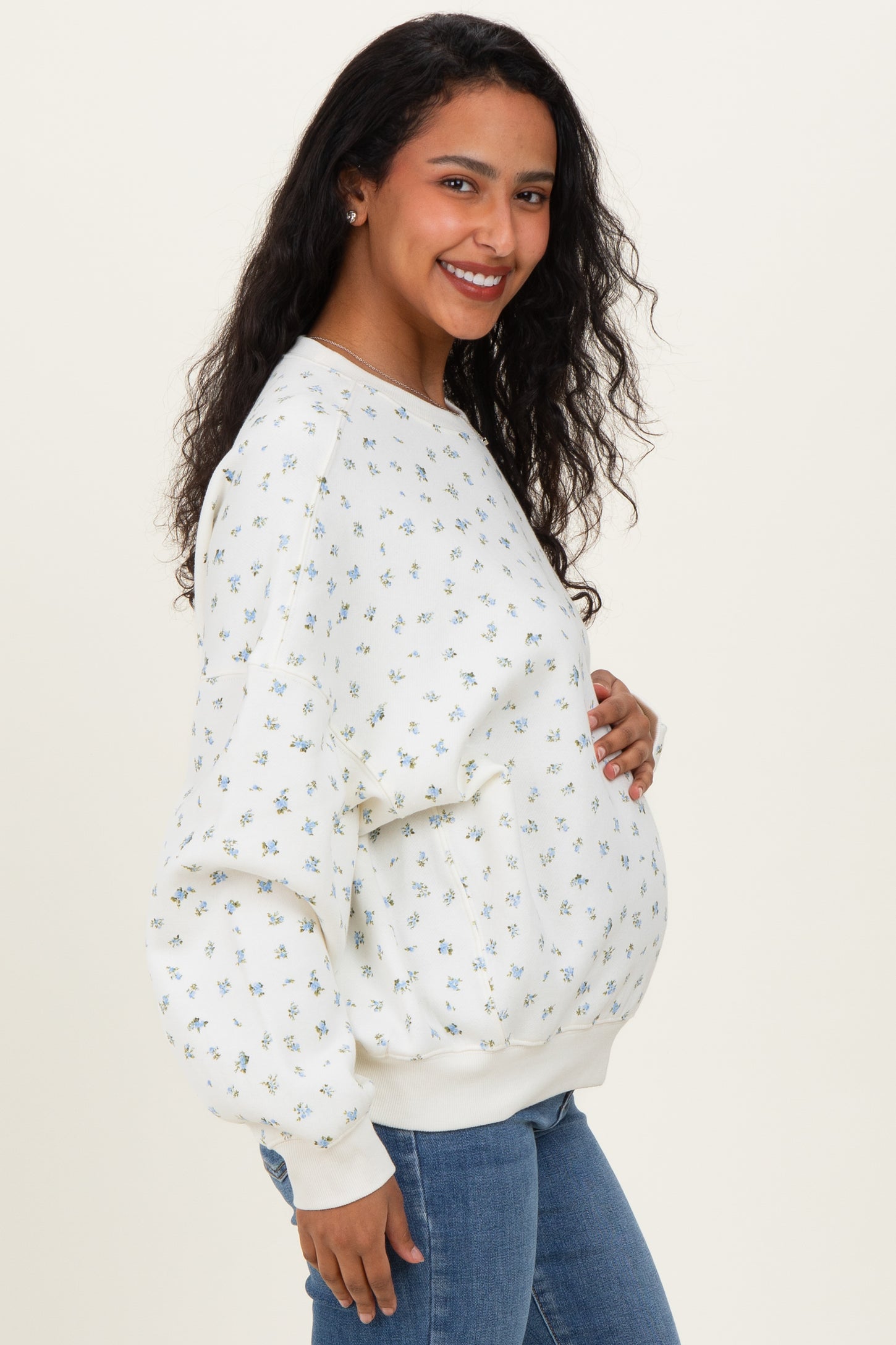 woman wearing a white maternity sweatshirt with floral print and a visible baby bump, paired with blue jeans