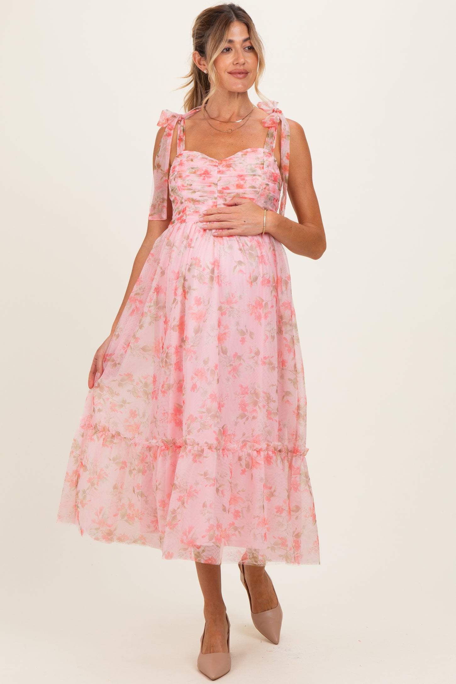 woman wearing a pink floral maternity dress with ruffled sleeves and a flowing skirt, showcasing her baby bump