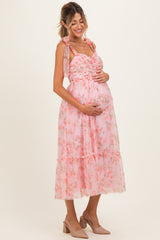 woman wearing a pink floral maternity dress with tie straps and holding her baby bump