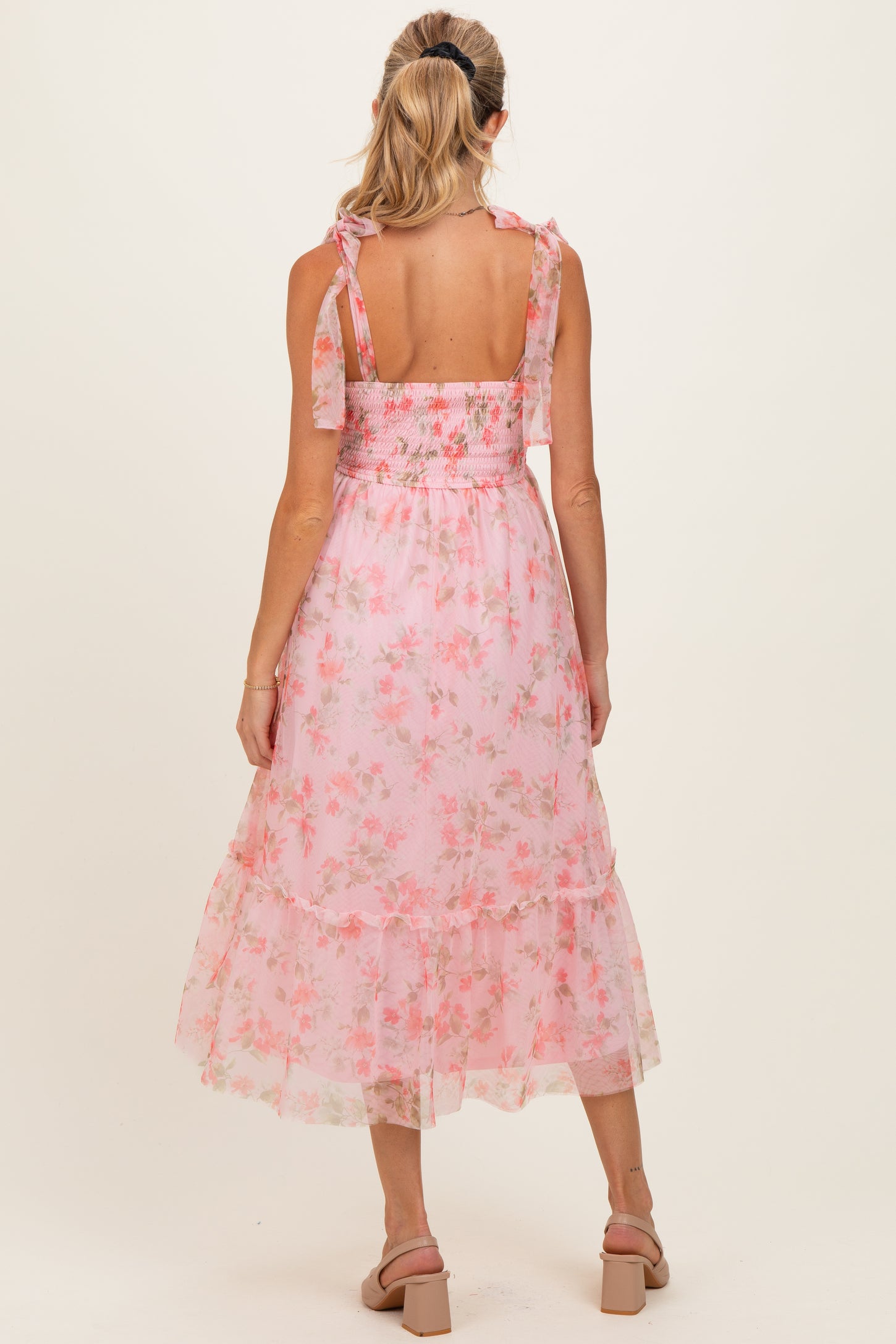 woman wearing a pink floral maternity dress with smocked bodice and ruffled hem, showing the back view