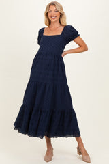 woman wearing a navy blue maternity dress with short puff sleeves and a tiered, embroidered skirt, showing her baby bump