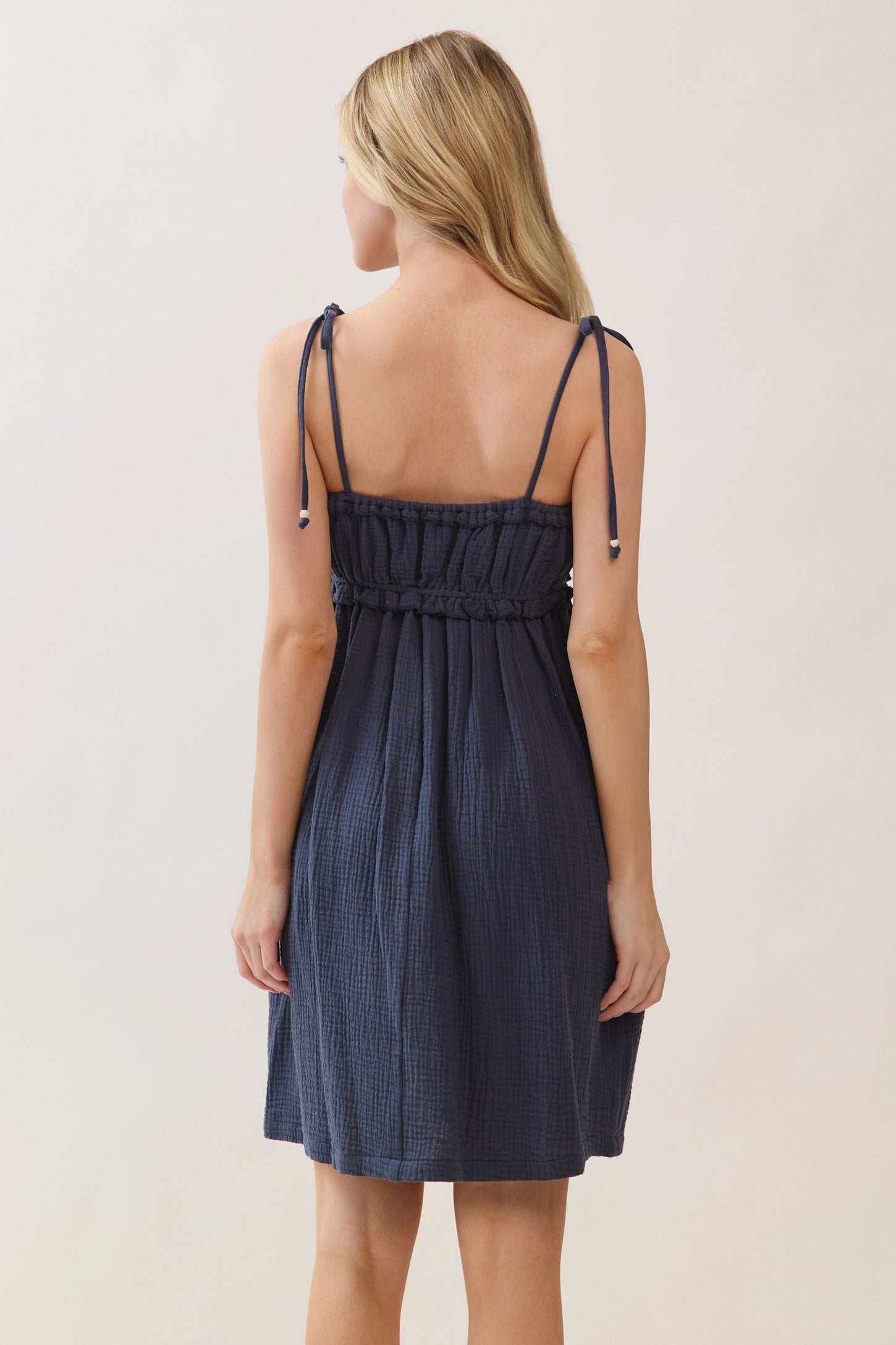 woman wearing a navy blue sleeveless dress with adjustable straps and a gathered waistline