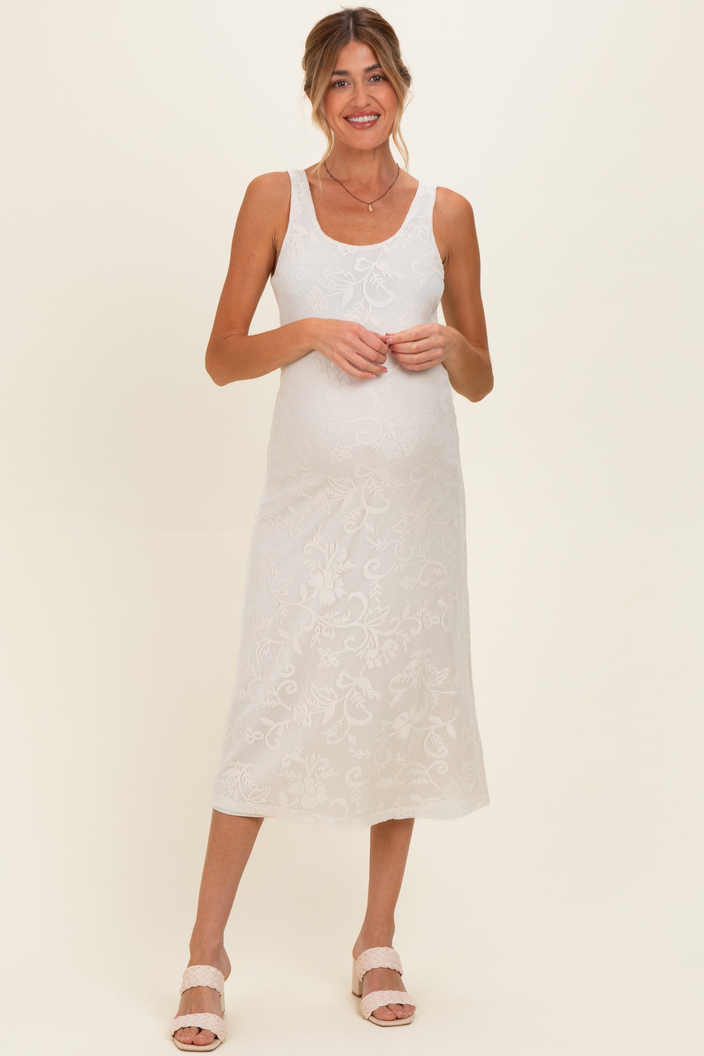 woman wearing a white floral lace maternity dress and showing her baby bump