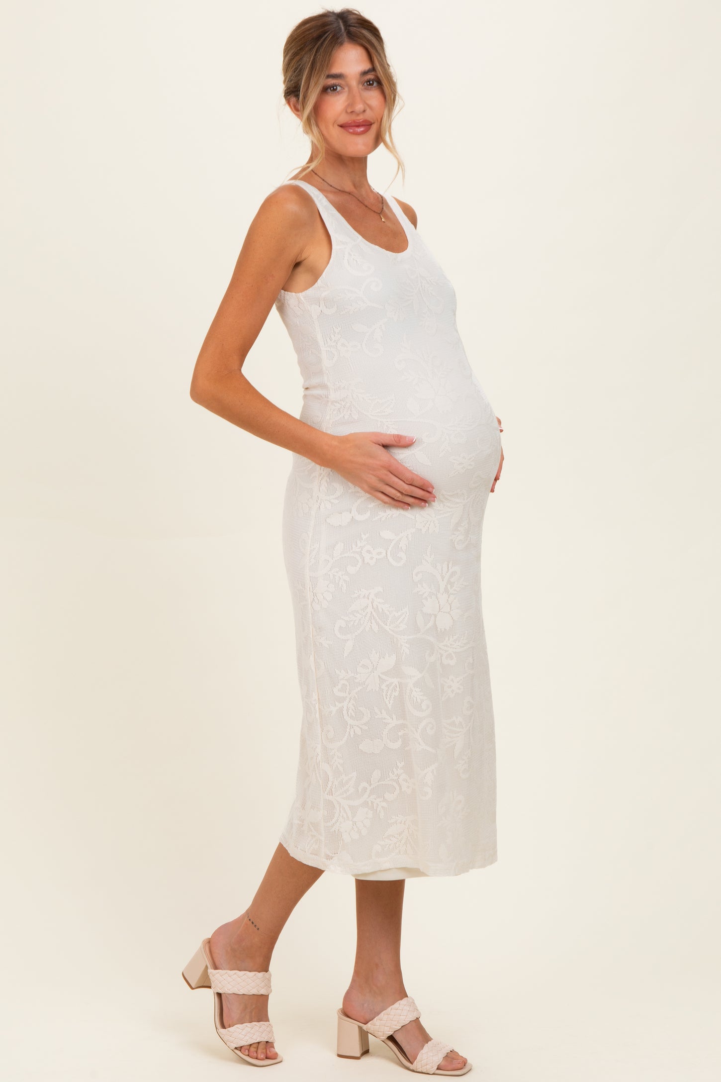 woman wearing a white lace maternity midi dress and gently cradling her baby bump