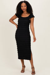 woman wearing a black midi dress with tiered ruffle details and short sleeves, standing with one hand on her hip