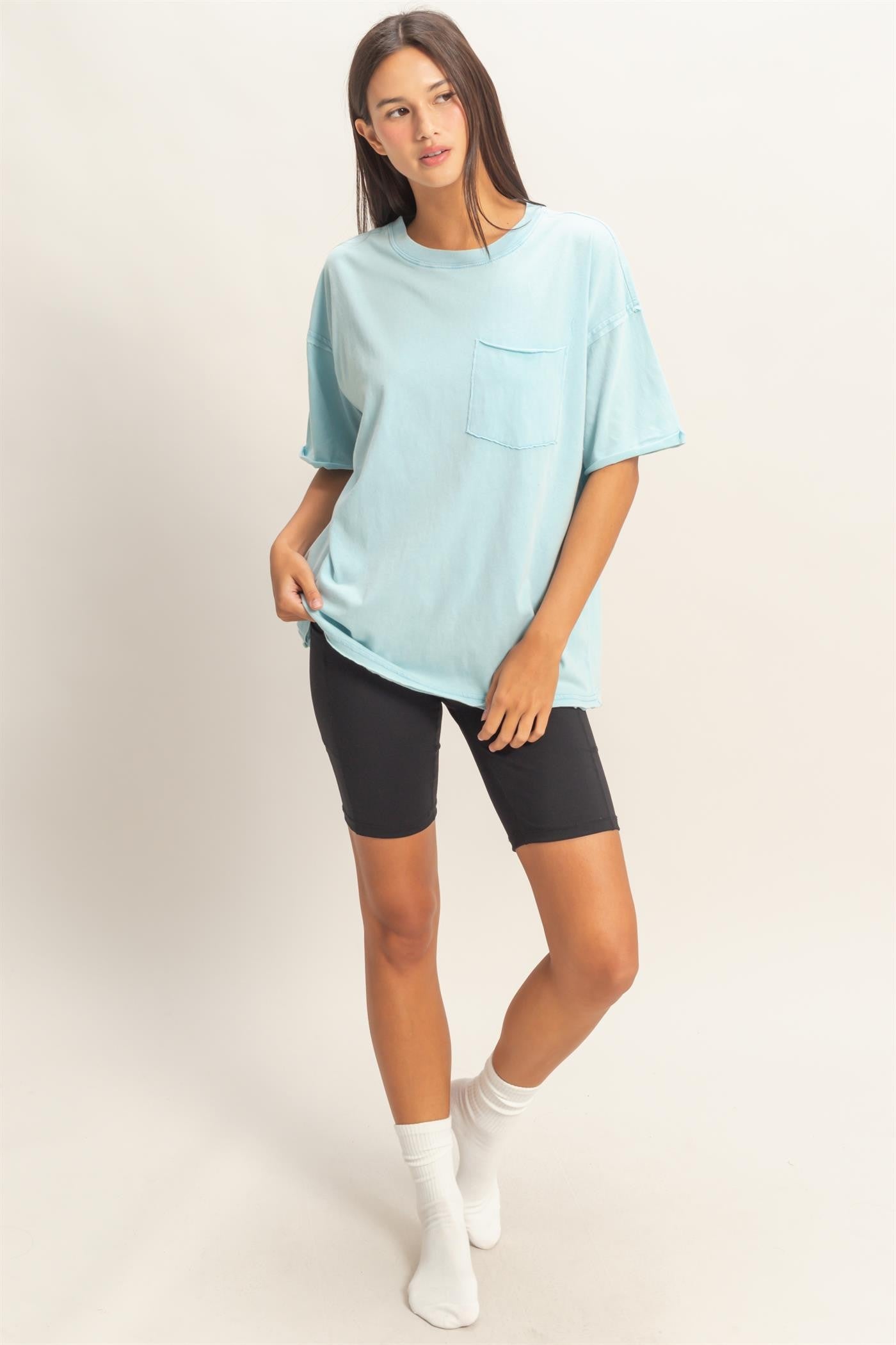 woman wearing a light blue oversized t-shirt with a pocket, paired with black bike shorts and white socks