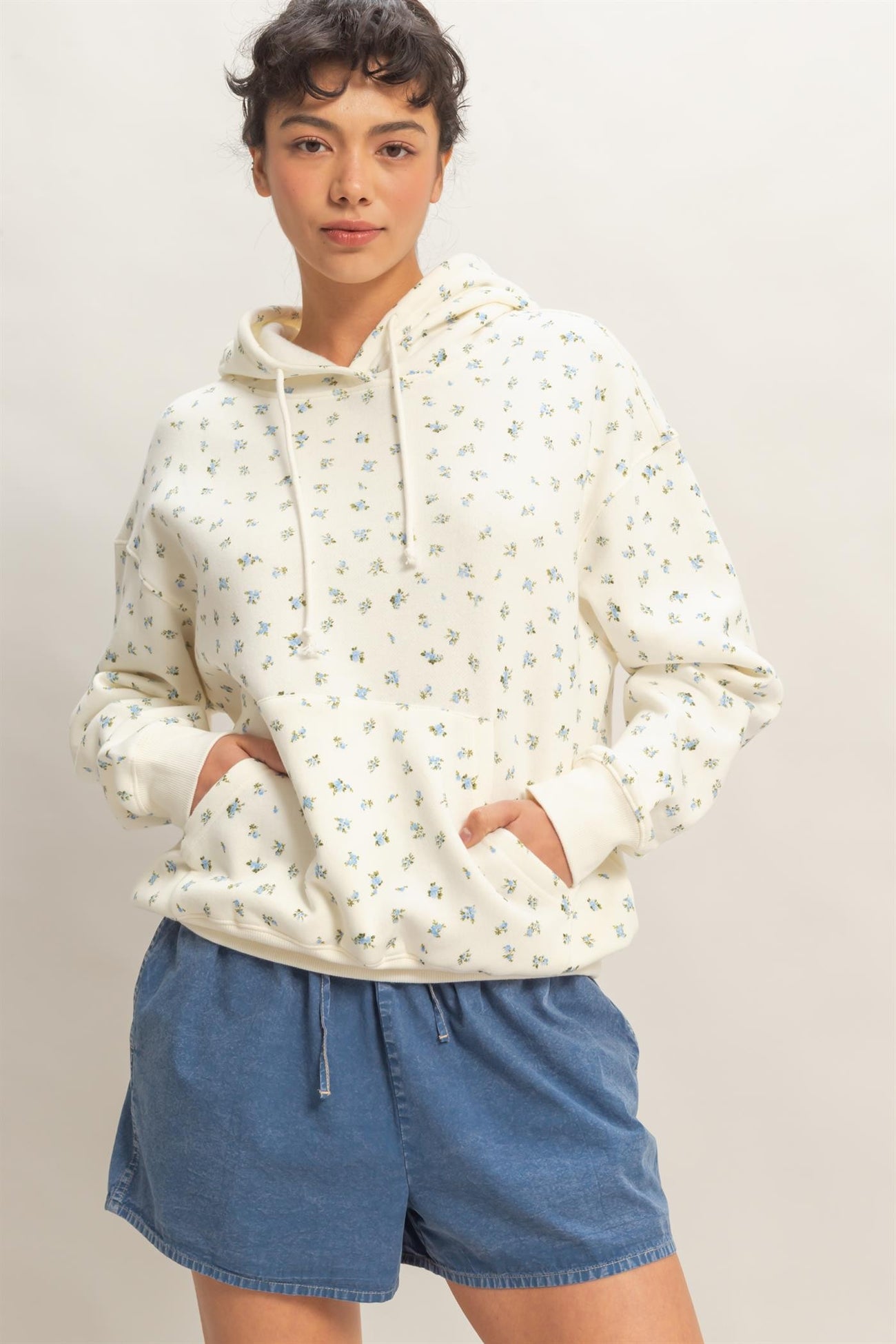 woman wearing a cream floral print hoodie with a front pocket and blue denim shorts