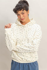 woman wearing a cream floral hoodie with a drawstring and long sleeves, posing with one hand on her shoulder