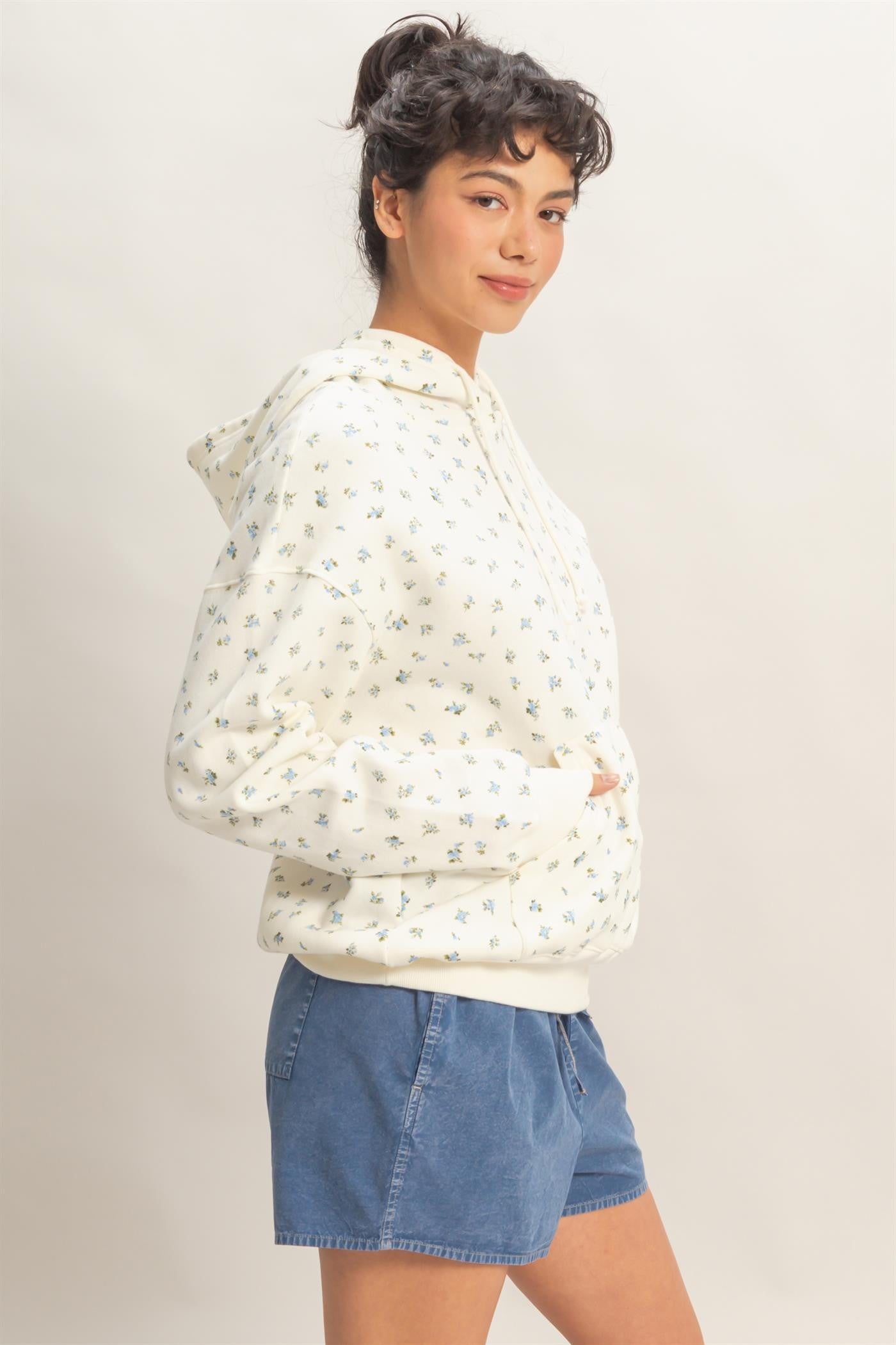 woman wearing a cream floral print hoodie with a front pocket and blue shorts