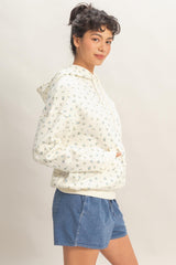 woman wearing a cream floral print hoodie with a front pocket and blue shorts