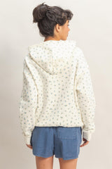 woman wearing a cream hooded sweatshirt with a floral print and denim shorts, showing the back view