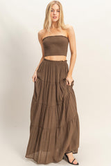 woman wearing a brown strapless smocked top and tiered maxi skirt, standing in a relaxed pose