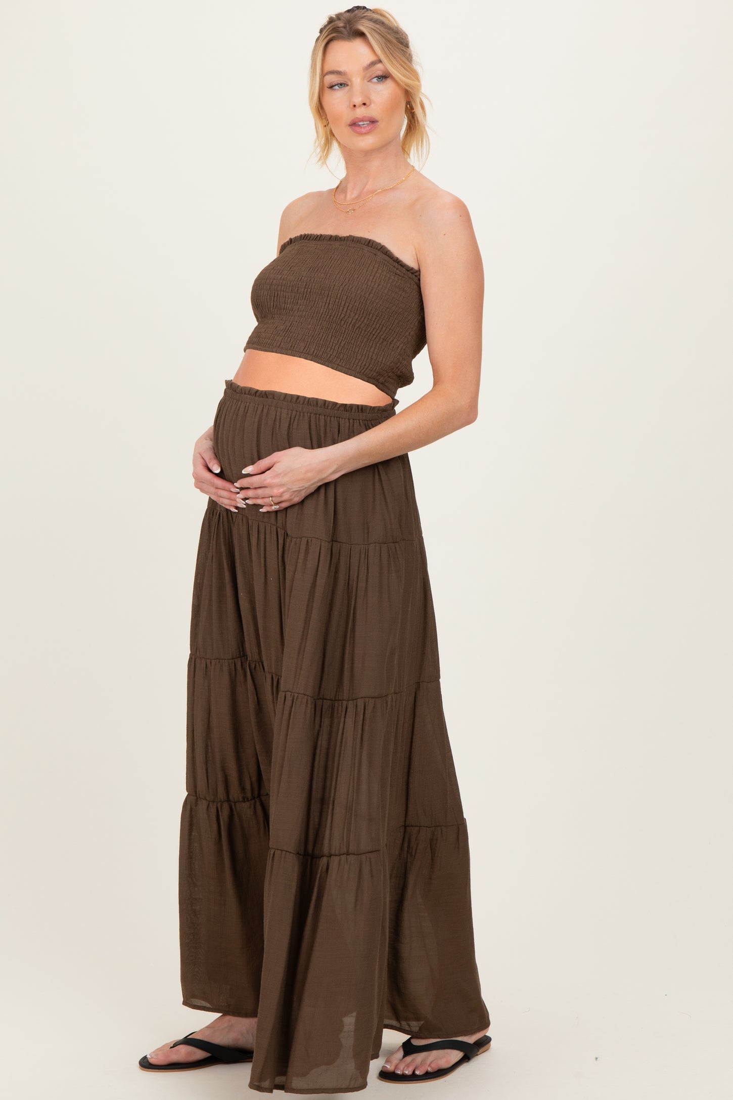 woman wearing a brown strapless maternity top and matching tiered maxi skirt, showing her baby bump
