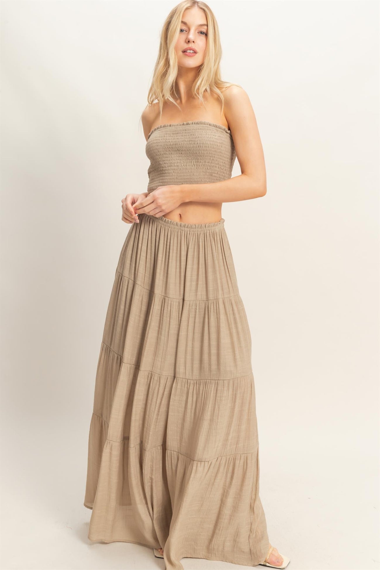 woman wearing a strapless beige tiered maxi dress with a smocked bodice and flowing skirt