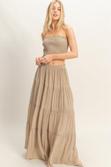 woman wearing a strapless beige tiered maxi dress with a smocked bodice and flowing skirt