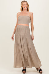 woman wearing a beige strapless smocked maternity crop top and matching maxi skirt, smiling with hands on hips