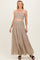woman wearing a beige strapless smocked maternity crop top and matching maxi skirt, smiling with hands on hips