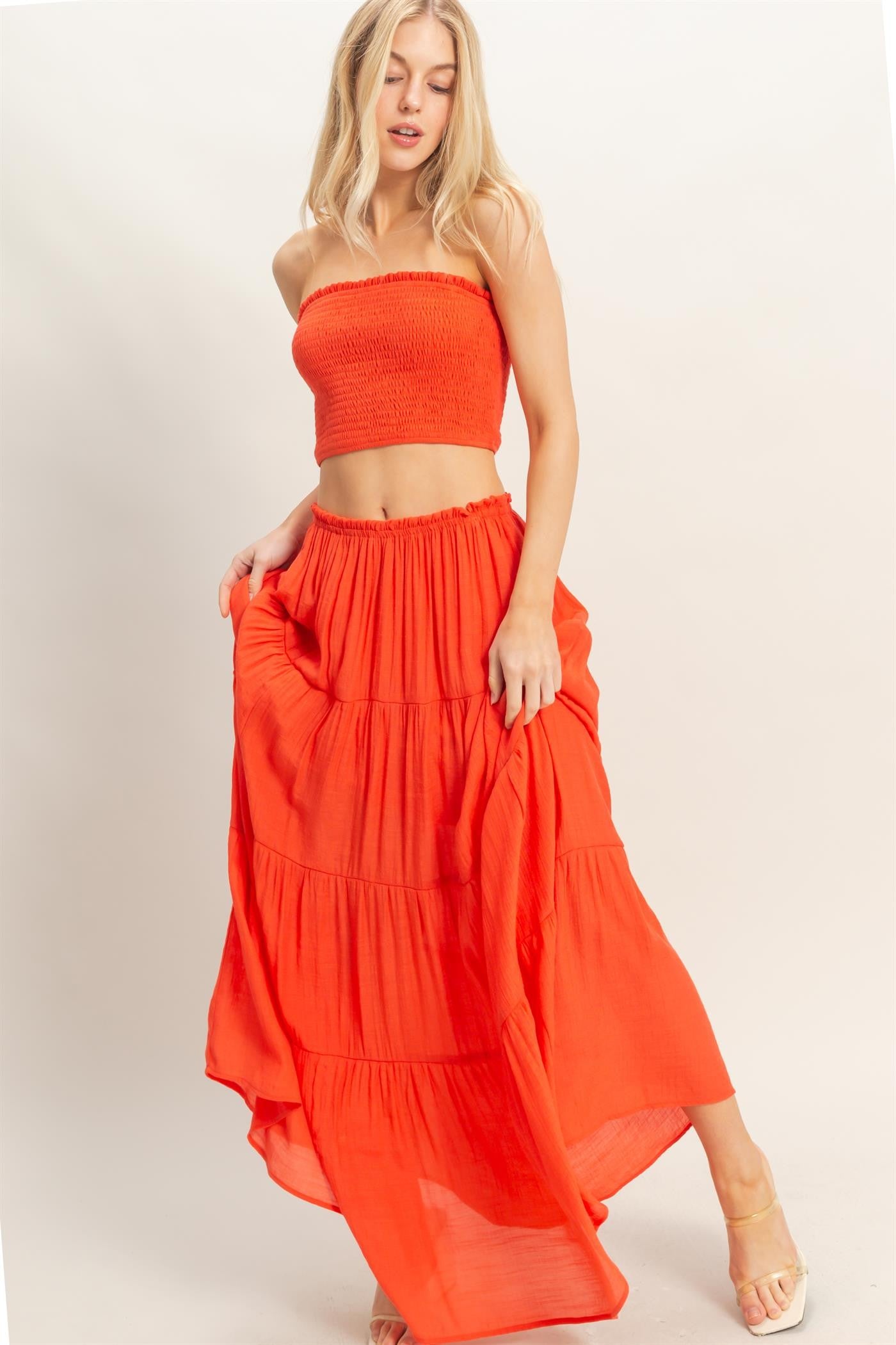 woman wearing a bright orange two-piece outfit with a smocked tube top and a tiered maxi skirt