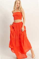 woman wearing a bright orange two-piece outfit with a smocked tube top and a tiered maxi skirt