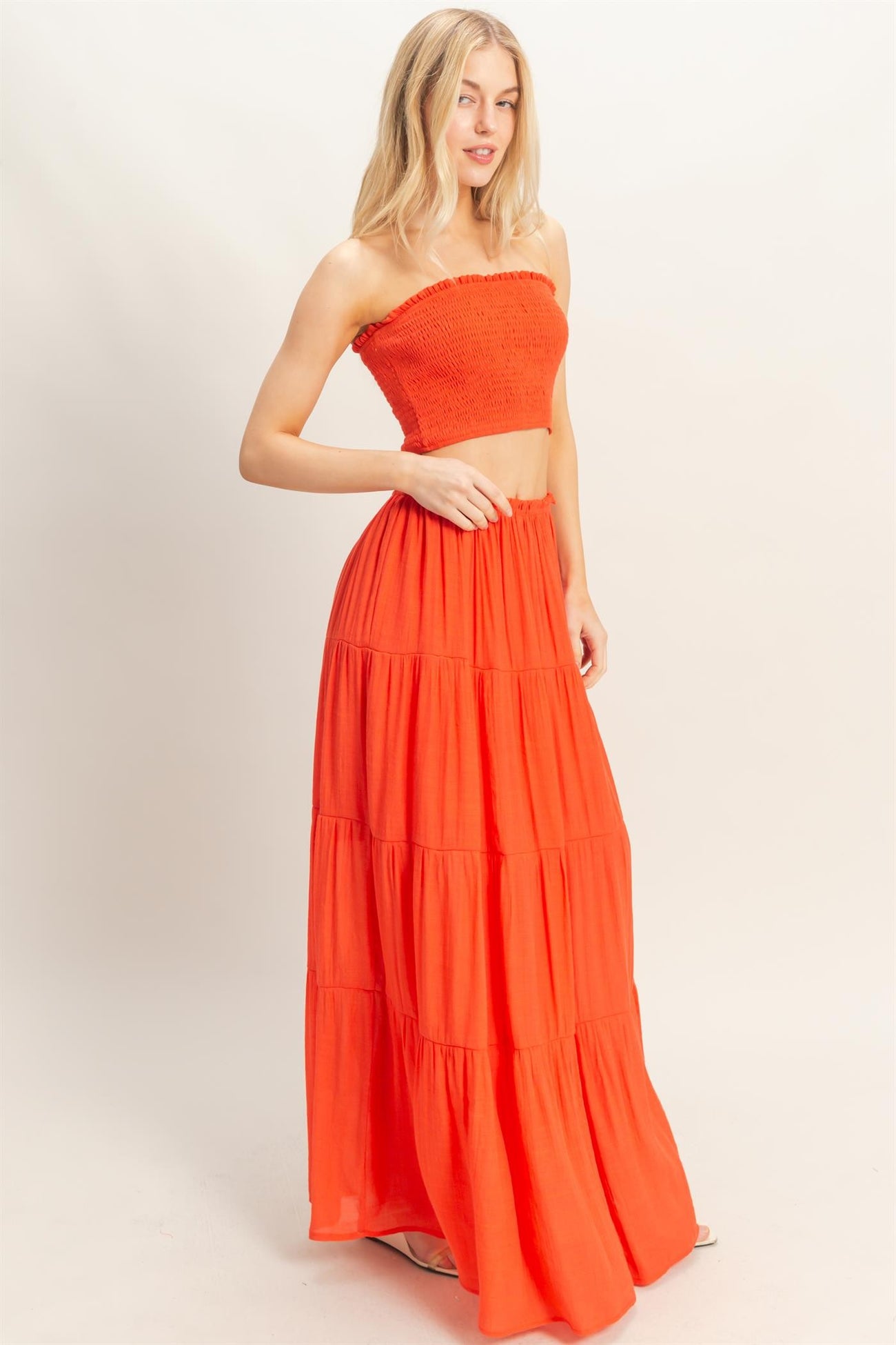 woman wearing a bright orange off-the-shoulder cropped top and a matching tiered maxi skirt