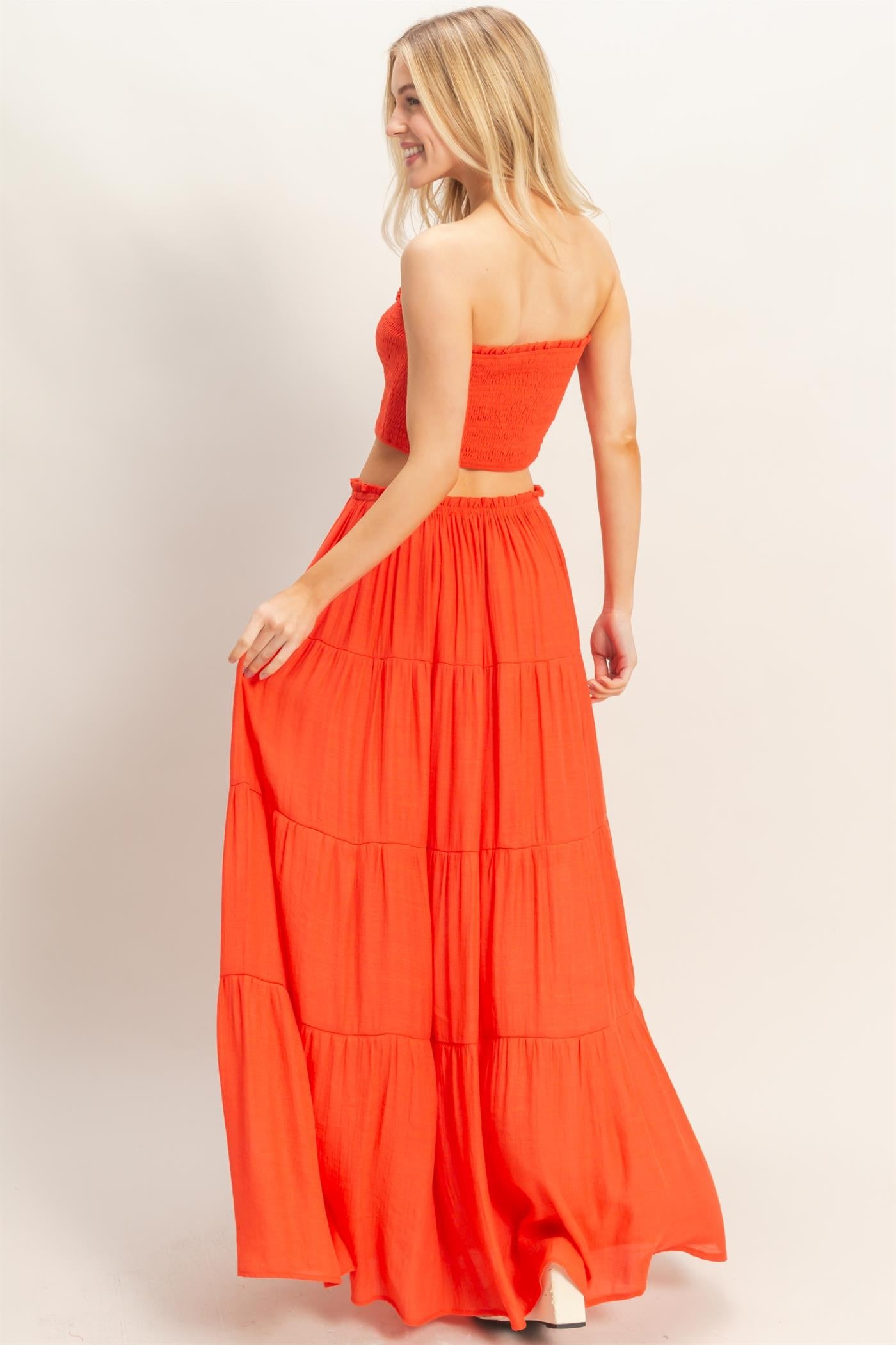 woman wearing an orange strapless top and a matching tiered maxi skirt, posing with her back to the camera