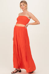 woman wearing a bright orange maternity two-piece set with a strapless top and a long tiered maxi skirt, showing her baby bump