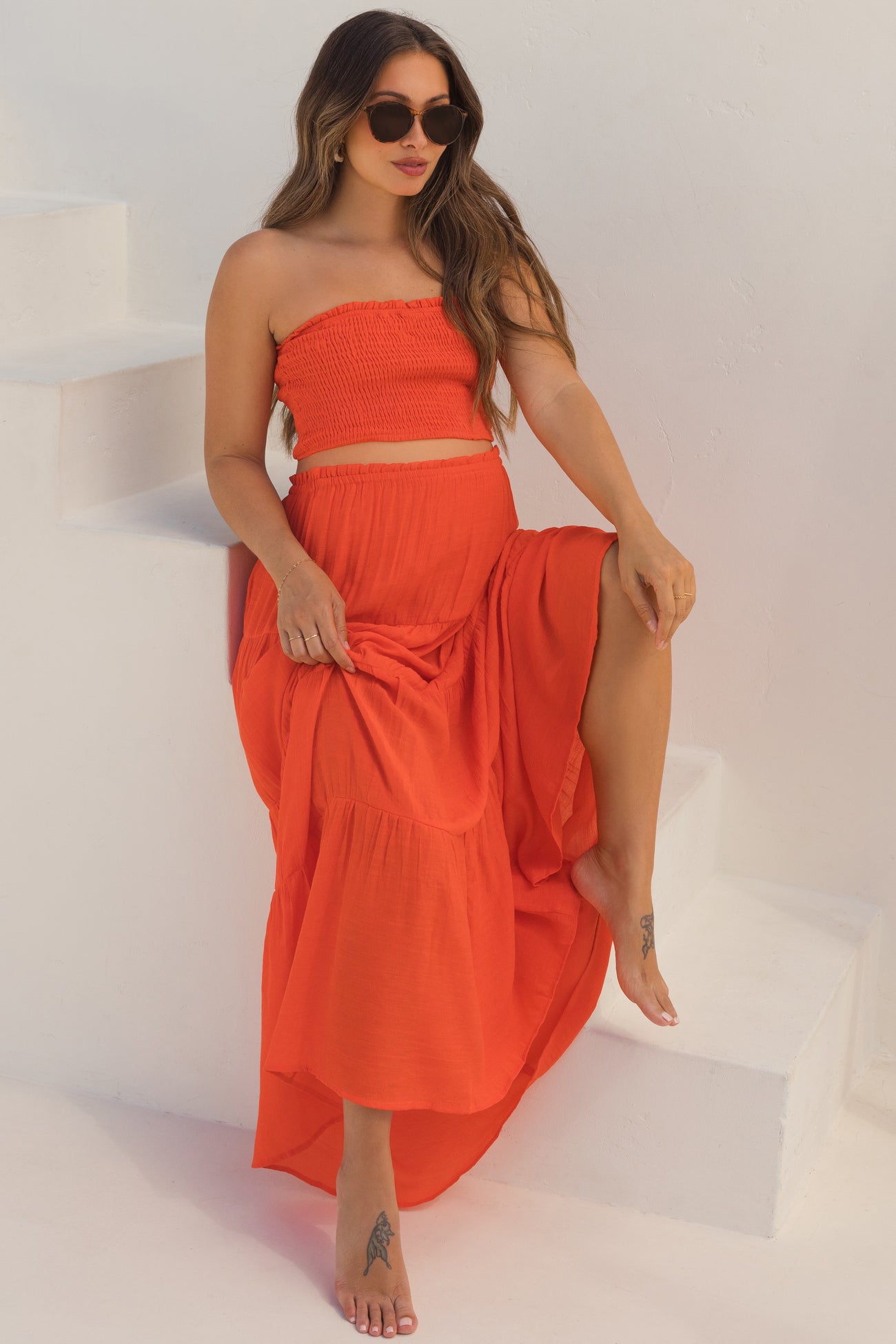 woman wearing a red strapless maternity top and matching maxi skirt, sitting on stairs with a baby bump visible