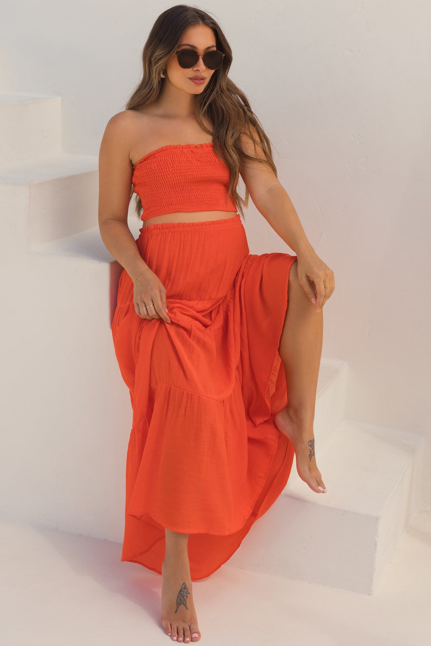 woman wearing a red strapless maternity top and matching maxi skirt, sitting on stairs with a baby bump visible