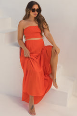 woman wearing a red strapless maternity top and matching maxi skirt, sitting on stairs with a baby bump visible