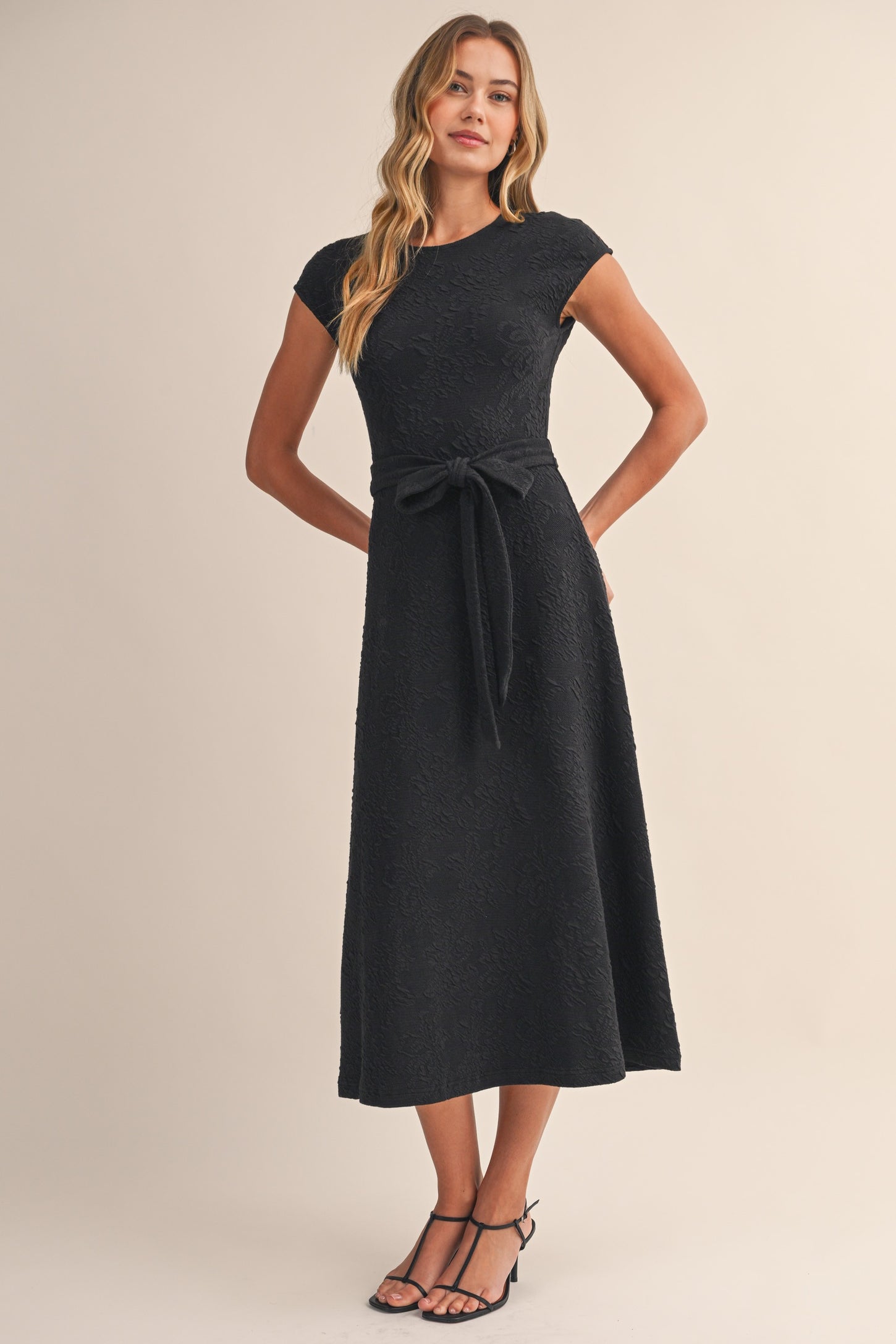 woman wearing a black cap sleeve belted midi dress with textured floral design