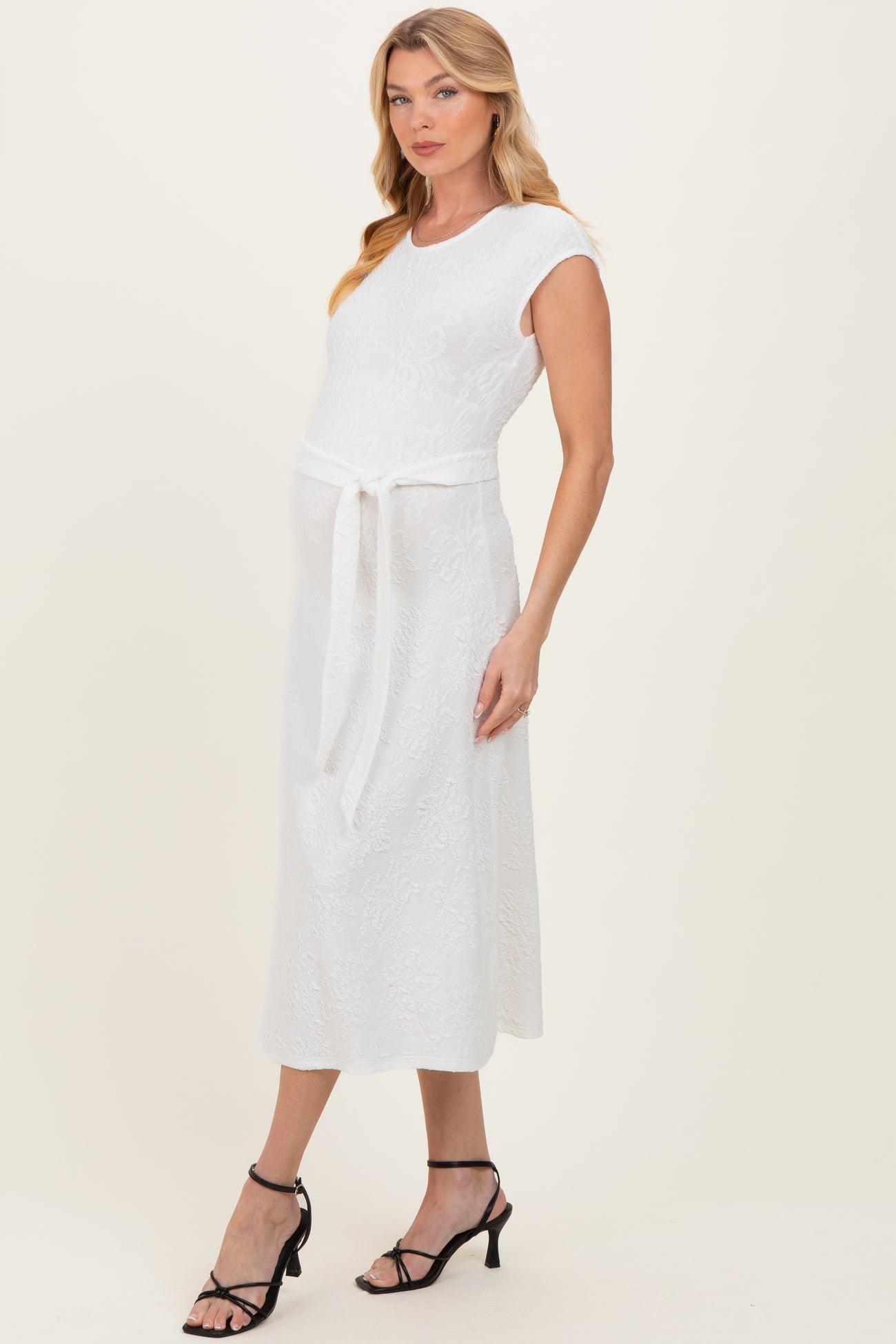 woman wearing a white maternity dress with a tie belt and short sleeves, showcasing her baby bump