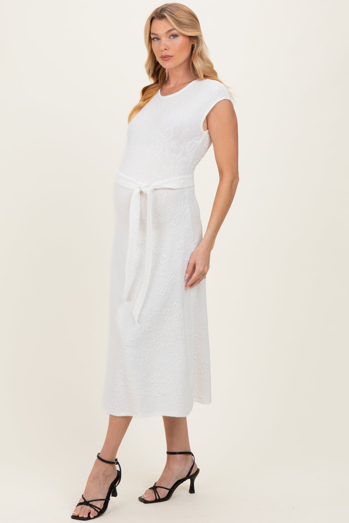 woman wearing a white maternity dress with a tie belt and short sleeves, showcasing her baby bump
