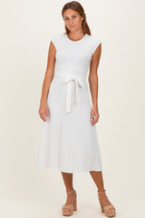 woman wearing a white cap sleeve midi dress with a tie waist and textured floral pattern, posing with a neutral backdrop