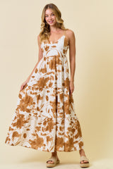 woman wearing a white maxi dress with brown floral prints and spaghetti straps, standing against a light beige background