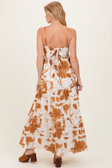woman wearing a maternity maxi dress with a floral print in brown and white, showing a tied back detail and flowing skirt
