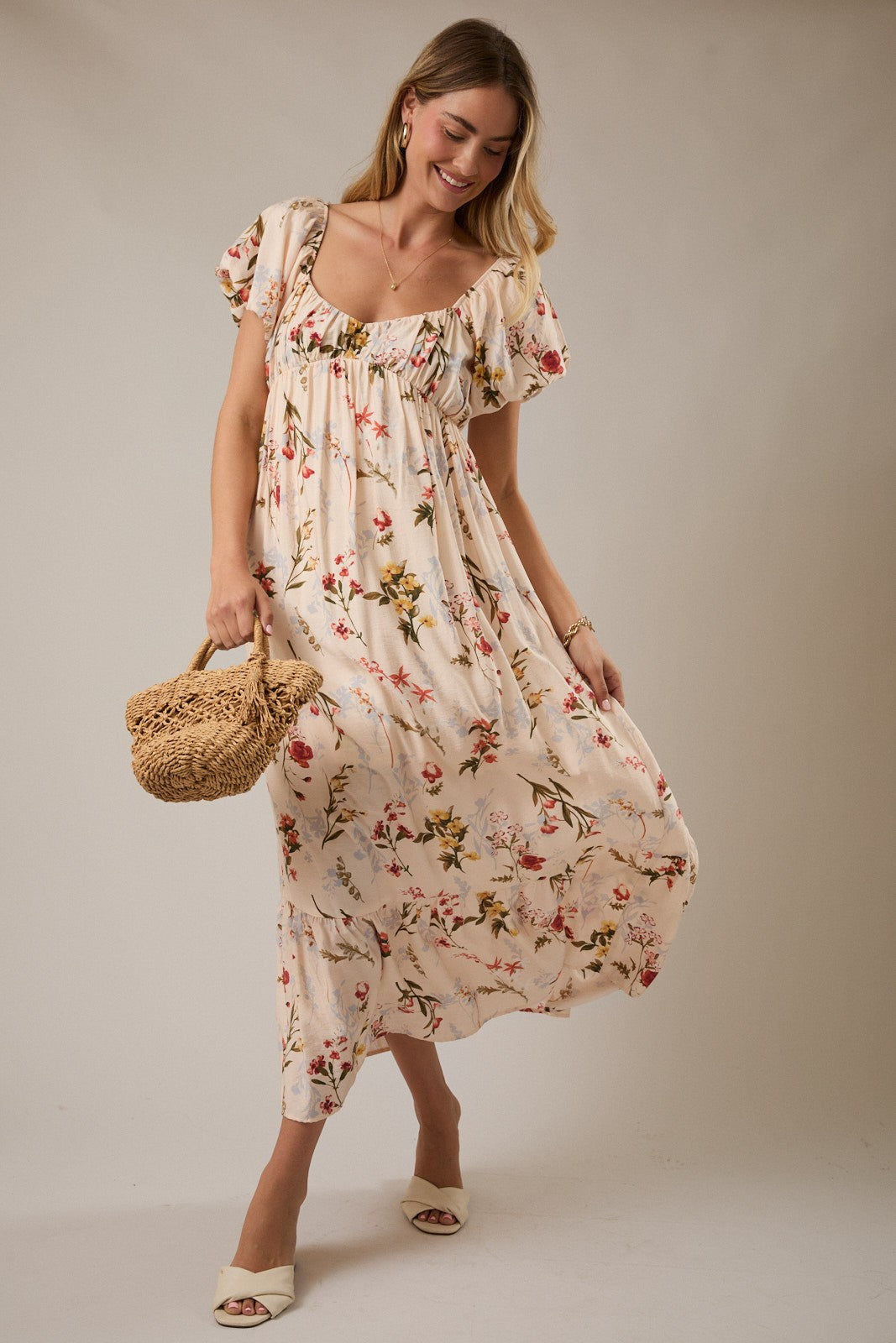woman wearing a floral printed maxi dress with puff sleeves and a gathered bodice, holding a straw bag
