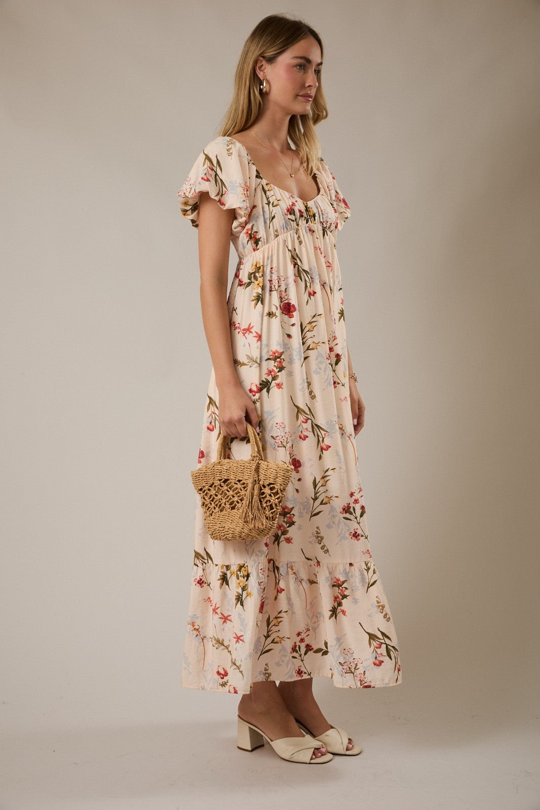 woman wearing a floral maxi dress with ruffled sleeves and holding a woven bag